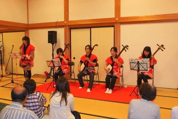 三味線を弾いている4名の方とマイクを持ち、立って歌っている女性の写真